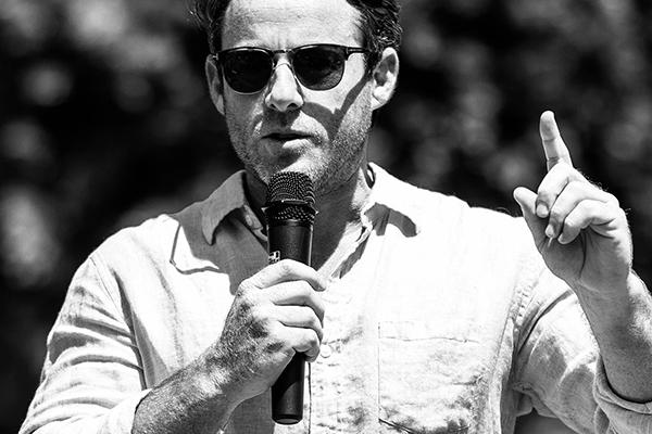 Jake Glaser, finger upraised, making a point as he holds a microphone while making a speech